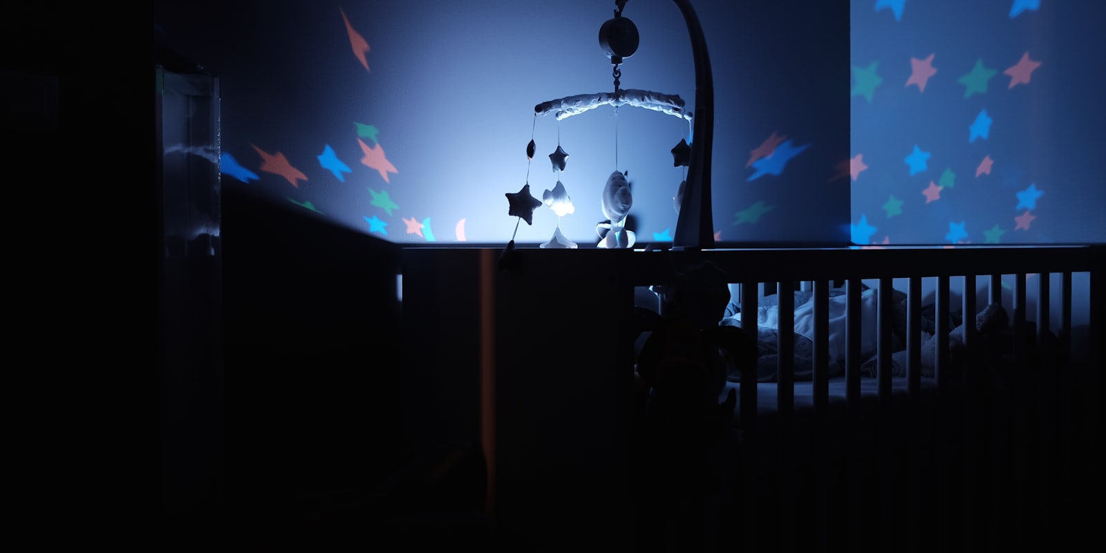 Veilleuse projetant des étoiles au-dessus d'un lit à barreaux dans une chambre de bébé la nuit